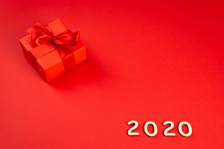 Christmas composition. Red gift box with a red ribbon on a red background and wooden numbers 2020....