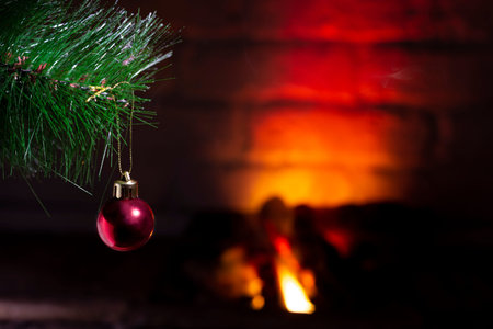 Red ball on a Christmas tree near a burning fireplace, close-up, Christmas composition.