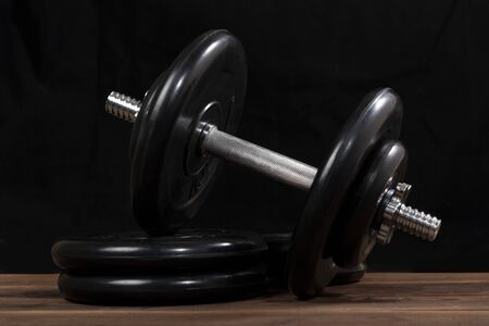 Big black male dumbbell on a brown wooden table on a black backgroundの写真素材