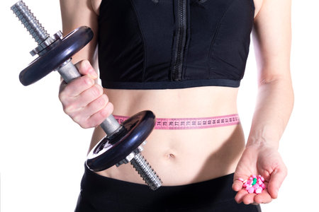 Sport and healthy woman holding dumbbells with measuring tape on the body and vitamins in hands.の写真素材