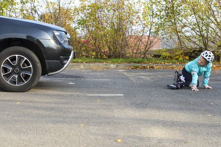 Belarus, Minsk, October 20, 2019. A little girl in a blue jacket and helmet on rollers fell in front of a moving car on a city street.のeditorial素材