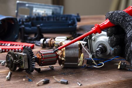 the master repairs a broken electrical device: drill, cutter on a wooden table. Electric Tool Repair Shopの写真素材