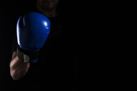 Men's hand in a blue boxing glove on a black background makes a punch - hook.の写真素材