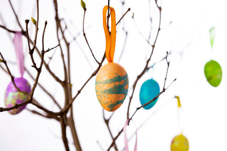 Colorful easter eggs hanging from tree branches on a light background.
