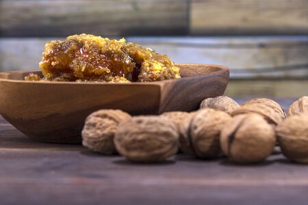 Honeycombs with honey in a wooden plate and many inshell walnuts on a wooden surfaceの写真素材