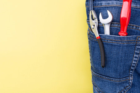 tools in the pocket of a craftsman jeans on a yellow background with place for text.