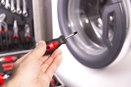 Repair and maintenance of the washing machine. Screwdriver in the hand of a master on the background of a washing machine.の写真素材
