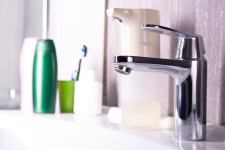 White washbasin and water tap. Contactless soap dispenser. Economical metal faucet and white ceramic...