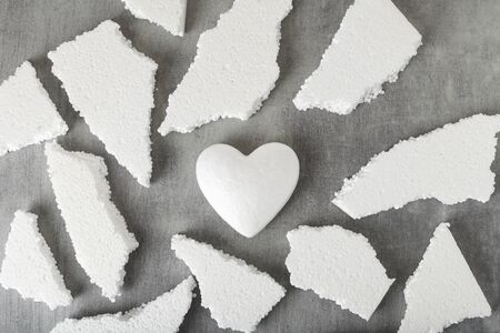 White polystyrene heart on a gray background, surrounded by fragments of polystyrene. Shards of a heart, a broken heart.の写真素材