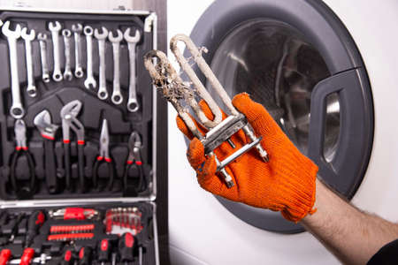 Repair of washing machines. Hand of a repairman with a turbulent electric heater covered with a coating of hard water. Replacing the electric heater in the washing machineの写真素材