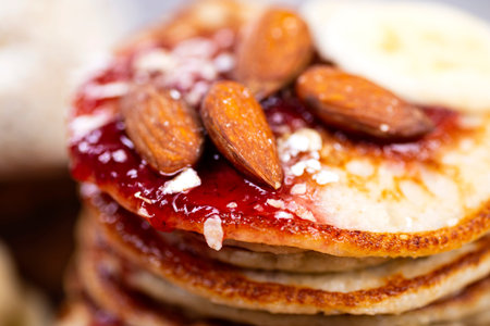 Stack of oat pancakes with jam and almonds in a wooden plate.