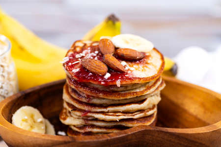 Stack of oat pancakes with jam and almonds in a wooden plate.の写真素材