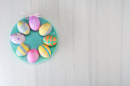 Colorful easter eggs on a turquoise plate on a gray table with place for text, top view.の写真素材