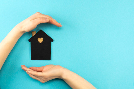Woman's hands surround a mock-up of a dark house on a blue background. Family, real estate and insurance concept, flat lay, top view.の写真素材