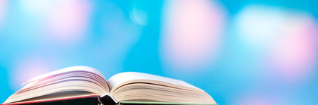 Opened old hardback book on a bright blue background with bokeh. Back to school. Space for text, banner photo.の写真素材