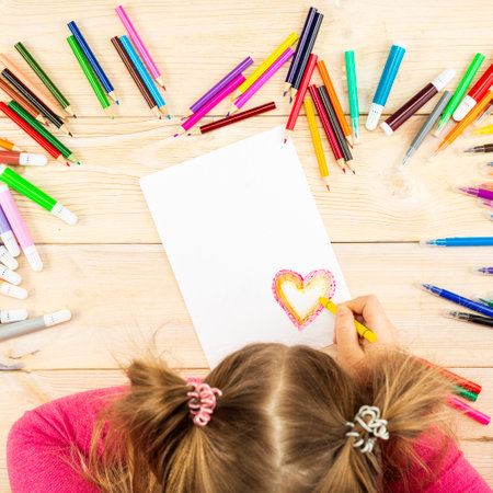 Little girl prepares cards with hearts for Valentine's Day. Drawing is done by a child with colored pencils or felt-tip pens. Child's drawing with place for text. View from above.の写真素材