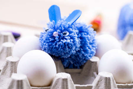 This blue rabbit is made of pompons for Easter decor by hand. Easter bunny and white eggs on a stand Children's art project. DIY concept.の写真素材