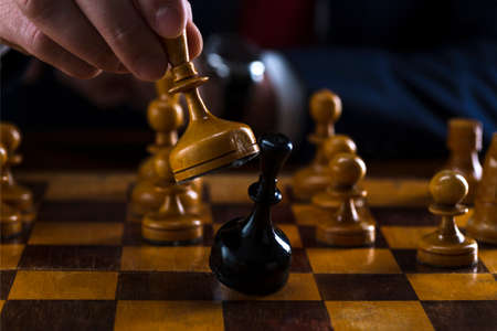 concept of strategy and business planning, businessman behind a chessboard white queen beats a black chess piece, strategy and tactics, readiness for battle, start of battle.の写真素材