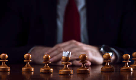 the concept of strategy and business planning, a businessman at a chessboard in front of lined up white pawns, one of which is in a paper crown, strategy and tactics, readiness for battle, the beginning of the battle.の写真素材