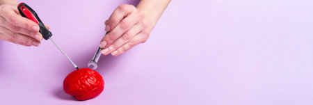 Hands fixing a model of a red brain with a screwdriver and a wrench on a pink background. Brain treatment. Fix the brain. Tools for repair.の写真素材