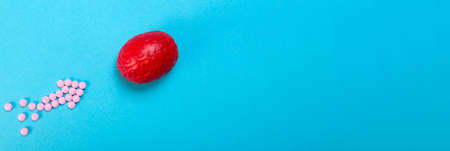 Red brain on a pink background with pink pills arranged in the form of an arrow. Brain pills. It is symbolic for drugs, psychopharmaceuticals, nootropics and other drugs. Brain treatment.の写真素材