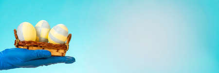 A hand in a medical glove holds a plate with colorful Easter eggs on a blue background.の写真素材