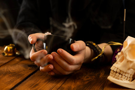 Fortune teller or oracle with holding a black cup for fortune telling on the coffee grounds. Psychic...