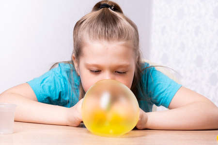 The blonde child inflates a bubble of yellow mucus. Play a slime toy. Making slime at home.の写真素材