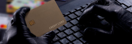 Internet Theft - Thief's Gloved Hands With Credit Card Behind Laptop.
