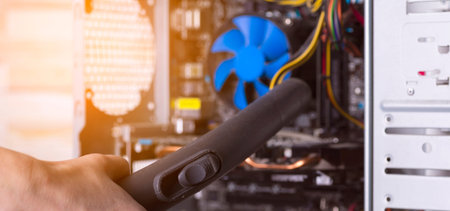 Cleaning the system unit of a desktop computer from dust with a vacuum cleaner.
