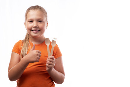 Cute caucasian little girl holding bamboo cutlery in her hands and showing thumbs up on a white...