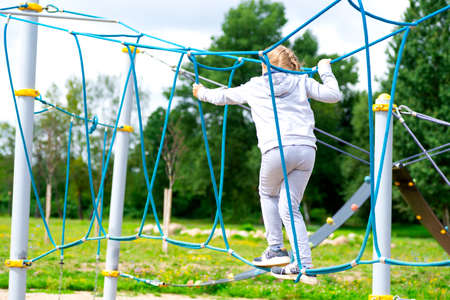 Little girl climbing in an adventure park. The girl loves to climb in the adventure of the rope course. Little girl on the rope obstacle course.の写真素材
