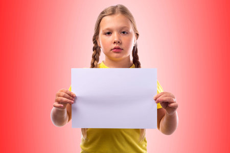 Cute serious girl with blond hair braided in a pigtail holding a white sheet of paper on a colored...