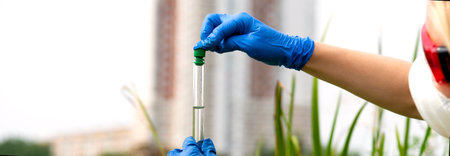 A gloved hand collects water into a test tube. Sampling from open water in a city water body....