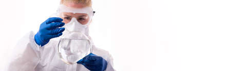 A woman in a chemical protection suit holds a flask with a chemical in front of her. Isolated on white background.の写真素材