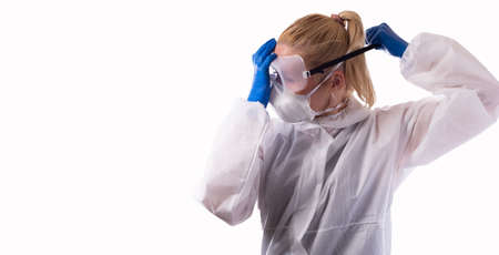 A woman in a chemical protection suit puts on goggles and regular equipment. Isolated on white background.の写真素材