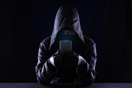 Hooded cyber crime hacker using mobile phone internet hacking in to cyberspace, online personal data security concept.の写真素材