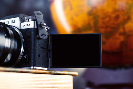 MINSK, BELARUS - OCTOBER 16, 2021: SILVER FUJIFILM X-T4 KIT XF16-80MM camera body with an open screen for viewing on an old book and a vintage globe in the background.のeditorial素材