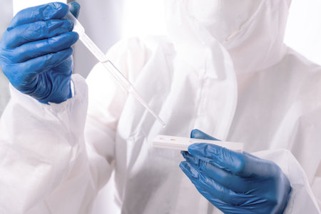Medical worker in a chemical protection suit with a pipette and a test strip on a white background.