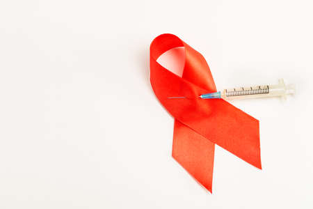 Health care and medicine concept. AIDS awareness. Red AIDS awareness ribbon pierced with injection syringe on white background. International AIDS Dayの写真素材