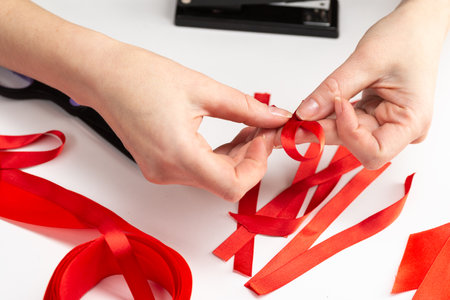 Health care and medicine concept. AIDS awareness. Female hands make red awareness ribbons with a red ribbon and a stapler. World aids dayの写真素材