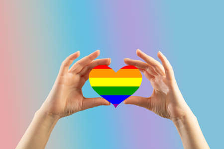 Female hands hold a rainbow heart on a blue background.の写真素材