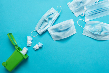 Throwing away a medical mask in a green container for recycling on a blue background. Blue face...