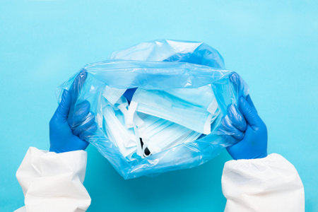 The hands of a man in gloves and a protective suit are holding a plastic bag with used medical...