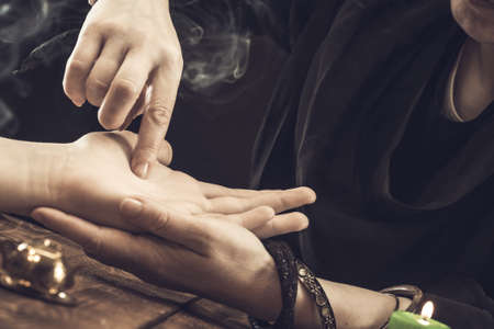 The witch is a fortune teller reading a good luck close-up. The fortune teller draws lines on the client's hand.の写真素材