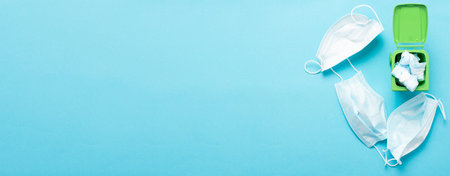 Medical masks in a green container for recycling on a blue background top view. Blue face masks...