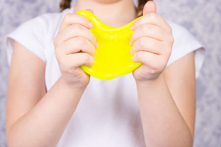The blonde-haired child is playing with mucus. Little beautiful caucasian girl is playing with yellow slime. Play Slime Toy.の写真素材