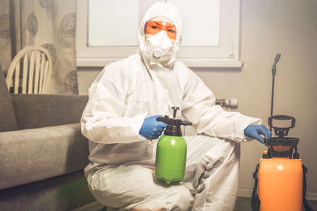 An exterminator in work clothes sprays pesticides with a spray gun. Fight against insects in apartments and houses. Disinsection of the premisesの写真素材