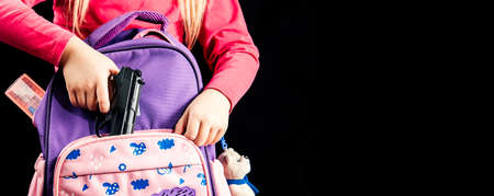 Girl hides a gun in a school backpack. Covert carrying weapons for protection. Weapons at school, assault at school, shooting.の写真素材