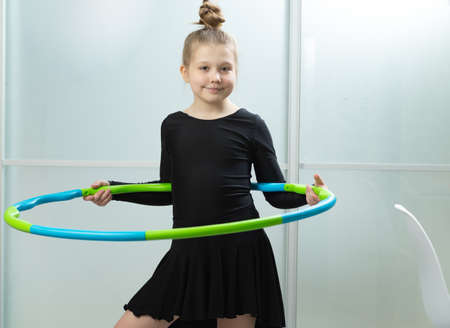 A child spins a hoop at home in the living room. Little girl with a dancing black dress twists a hoop at home in the living roomの写真素材